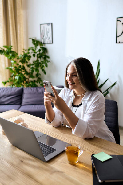 Женщина с синдромом Варденбурга улыбается, работая из дома на ноутбуке и телефоне.