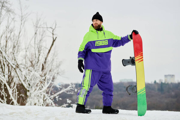Бородач готовится к сноуборду на зимнем склоне, одетый в разноцветную одежду..