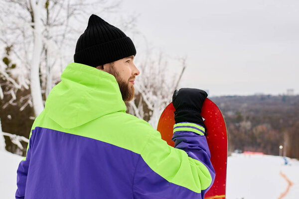 Бородатый человек в яркой экипировке готовится к сноуборду по снежному склону.
