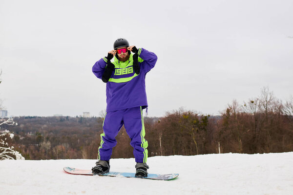 A man with a beard snowboards on a snowy slope, dressed for winter sports.