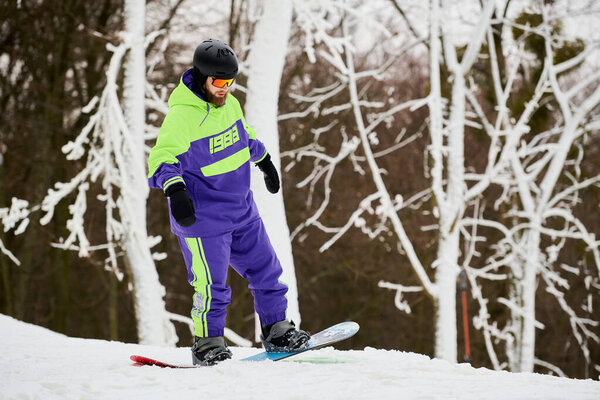 Человек с бородой катается на сноуборде по снежному склону, окружённому деревьями.