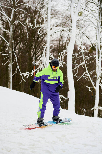 A bearded man skillfully snowboards down a snowy slope surrounded by trees on a winter day.