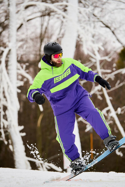A bearded man skillfully snowboards on a white slope under a clear winter sky.