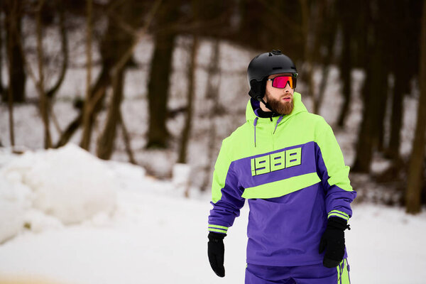 A bearded man snowboards down a snowy slope wearing vibrant outerwear, embracing the winter spirit.