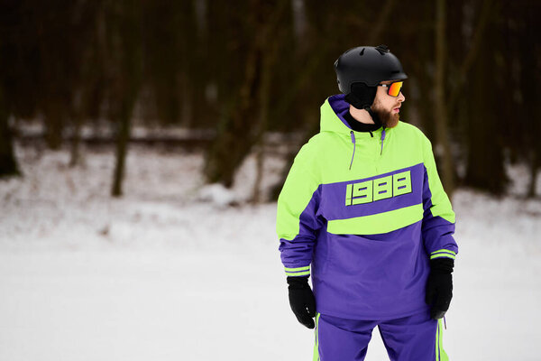 A bearded man enjoys snowboarding on a snowy slope, showcasing his skills in bright winter gear.
