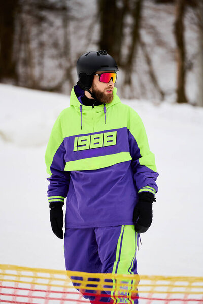 A bearded man rides down a snowy slope, showcasing his snowboarding skills in bright gear.