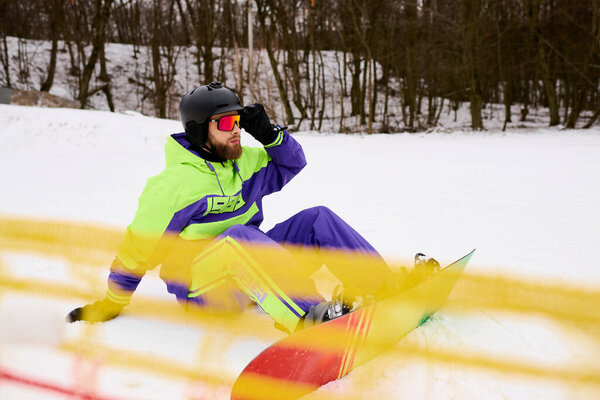 Бородатый человек в яркой экипировке сноубордист по снежному склону, сосредоточенный и активный.