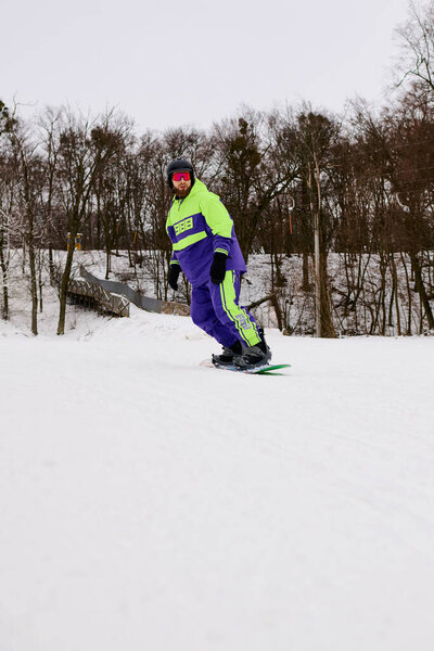 Сноубордист с бородой наслаждается захватывающей поездкой на снежном склоне, окруженном деревьями.
