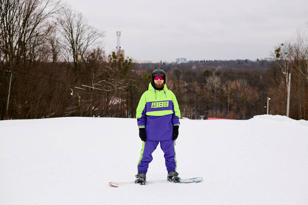 Бородач любит кататься на сноуборде по снежному склону в разноцветной зимней одежде.