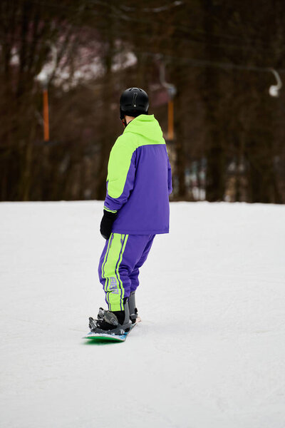 A sportsman rides down a snowy slope, showcasing his snowboarding skills in bright attire.