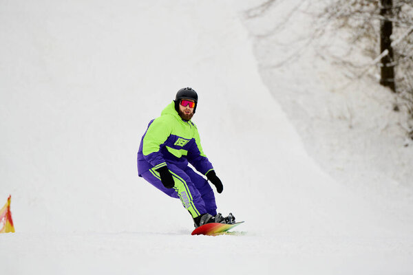 A bearded man skillfully snowboards down a snowy slope, enjoying the winter chill.