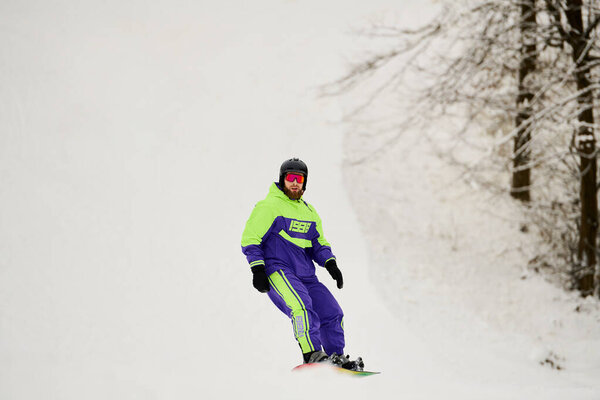 Человек с бородой умело катается на сноуборде по снежному склону, наслаждаясь зимними видами спорта.