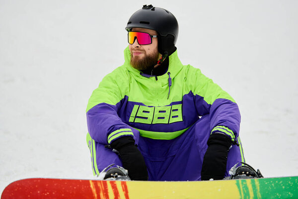 A bearded man takes a moment on a snowy slope, preparing to snowboard amidst winter surroundings.