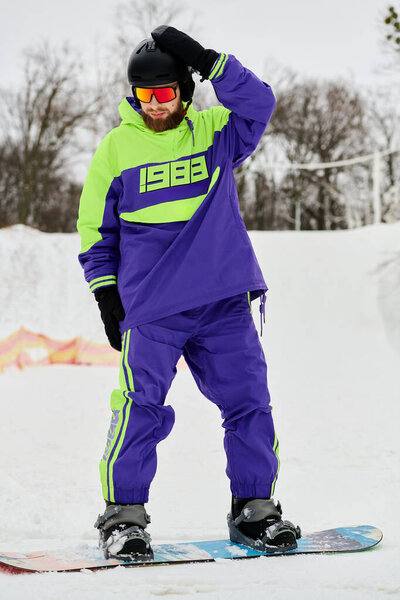 Бородатый мужчина в яркой верхней одежде наслаждается зимним холодом во время сноуборда на склоне.