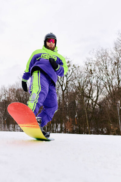 Бородач катается на сноуборде по снежному склону в яркой верхней одежде зимой.