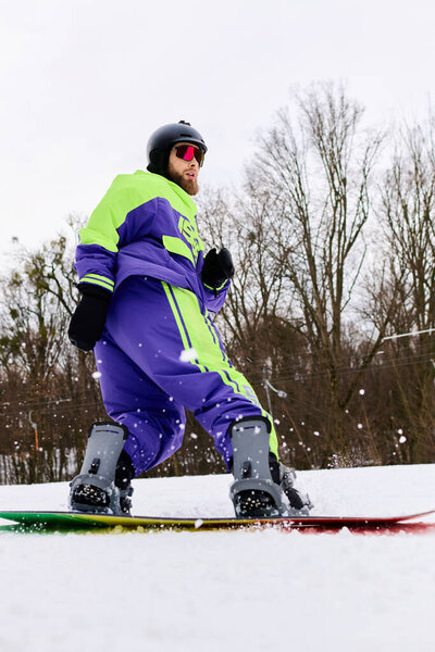 Опытный сноубордист в яркой верхней одежде перемещается по снежному склону, увлекаясь зимними видами спорта..