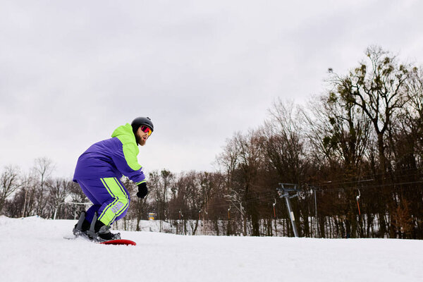 Бородач умело катается на сноуборде по заснеженному склону в зимний день..