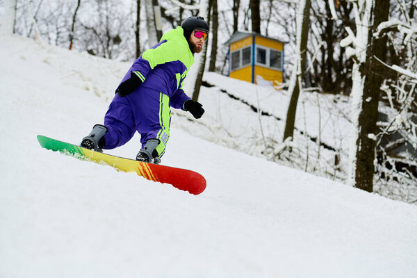 На заснеженном склоне сидит бородатый мужчина, наслаждающийся сноубордом в разноцветной одежде.