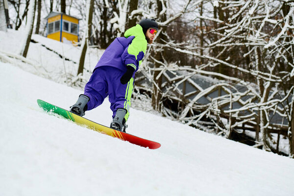 Бородач умело катается на сноуборде по снежному склону, демонстрируя яркую зимнюю экипировку..