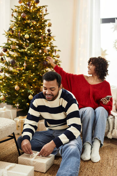Счастливая пара наслаждается Рождеством вместе, упаковывая подарки у своей очаровательной елки в уютном доме.