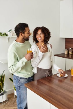 Neşeli bir Afrikalı Amerikalı çift hamileliğini sıcak mutfaklarında atıştırmalık ve içeceklerle kutluyor..