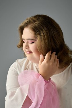 Down sendromlu genç bir kadın neşeli bir şekilde saçlarına dokunarak nazikçe gülümsüyor..