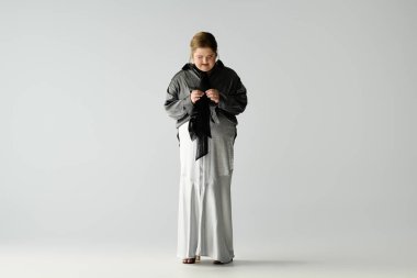 Genç bir kadın, kıyafetlerini stüdyoda gülümseyerek düzeltirken şık bir kıyafetle mutluluğunu ifade ediyor..