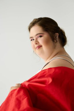 Down sendromlu genç bir kadın neşe saçıyor, elinde parlak kırmızı kumaş tutuyor..