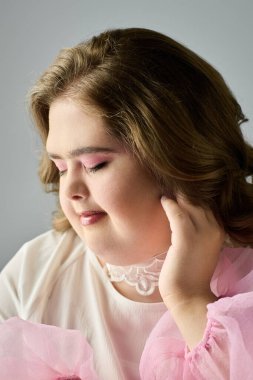 Down sendromlu neşeli genç bir kadın hoş pembe bir kıyafet giyerken hafifçe gülümsüyor..