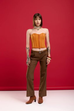 Turuncu giysili şık bir genç kadın dikkat çekici bir kırmızı arka planda duruyor..