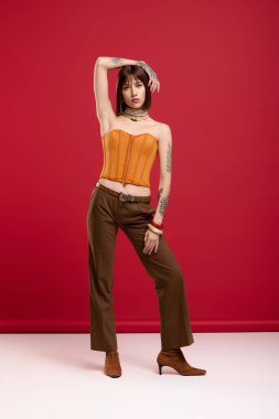 Kendine güvenen genç bir kadın, koyu turuncu bluzu ve şık kahverengi pantolonuyla modern moda sergiliyor.