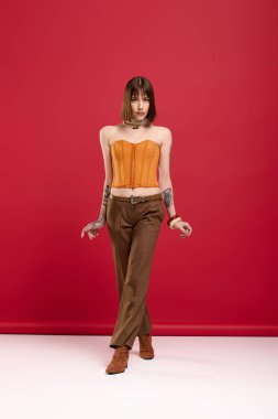 Zarif genç bir kadın, parlak kırmızı bir duvara karşı şık bir elbise içinde poz verir..