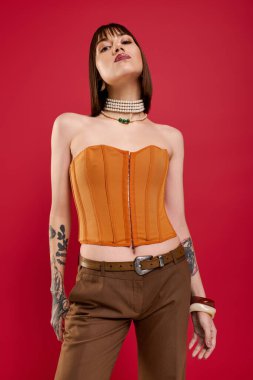 Kendine güvenen genç bir kadın dikkat çekici kırmızı bir arka planda kendine has tarzını gösteriyor..