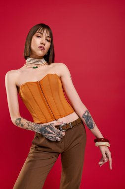 Genç ve güzel bir kadın canlı kırmızı bir arka planda dövmeli şık elbisesini sergiliyor..