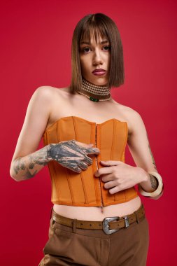 Kalın turuncu korseli ve şık aksesuarlı genç kadın kendinden emin duruyor..