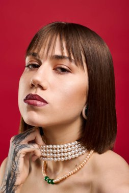 Şık giyinmiş, dövmeli, parlak kırmızı bir arka planda kendine güvenen genç bir kadın..