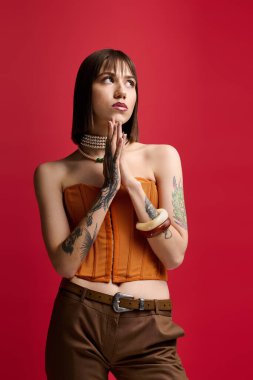 Zarif genç bir kadın zarif bir şekilde kırmızı bir zemine karşı poz veriyor, büyüleyici ve zarif..