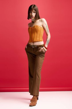 Genç kadın dikkat çekici turuncu bluz ve şık kahverengi pantolon giyerek moda sergiliyor..