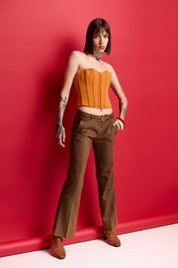 Kendine güvenen genç bir kadın, çarpıcı bir kıyafetle kırmızı bir zemine karşı poz veriyor..