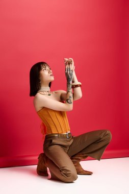 Şık giyinmiş genç, güzel bir kadın diz çöker, zarafet ve cazibe saçar..