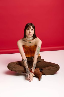 Şık bir genç kadın kendine güvenerek poz veriyor. Parlak bir ortamda sanatsal dövmeleri var..