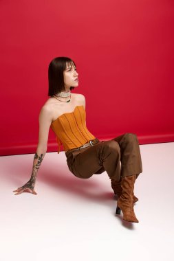 Yerde zarif bir şekilde oturan genç bir kadın şık kıyafetini ve özgüvenini sergiliyor..