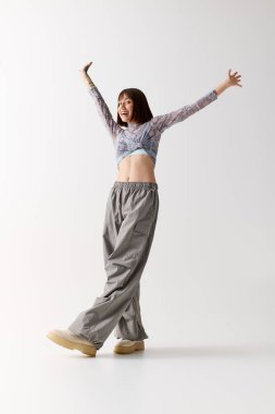 Genç bir kadın coşkulu tarzını sergilerken mutlu bir şekilde parlak bir mekanda poz veriyor..