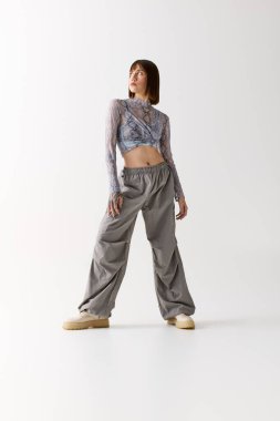 Tarz sahibi genç bir kadın, asgari dekor ile çevrili, modaya uygun giysiler içinde duruyor..