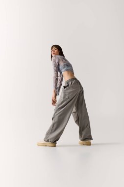 Şık giyinmiş güzel bir genç kadın minimalist bir stüdyo ortamında rahatça poz veriyor..