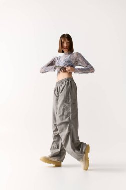 Şık giyinmiş genç bir kadın, parlak bir stüdyoda kendine güvenerek poz veriyor..