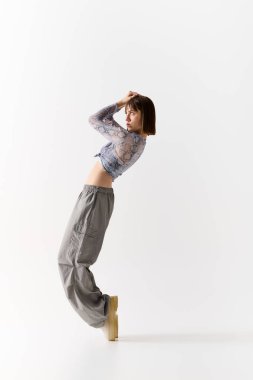 Güzel genç bir kadın zarif bir şekilde duruyor, temiz bir alanda şık moda kıyafetlerini sergiliyor..