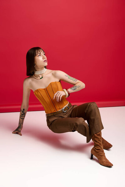 Young woman in a chic outfit poses against a bold red backdrop, displaying her sense of style.