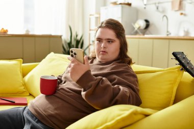 Genç bir kadın evdeki parlak sarı koltukta dinleniyor, kırmızı bardaktan yudumluyor ve mesajlaşıyor..