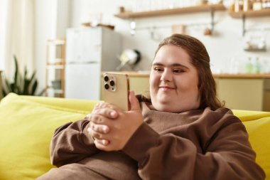 Down sendromlu genç bir kadın evinde akıllı telefonunu kullanırken gülümsüyor. Mutluluk dolu..